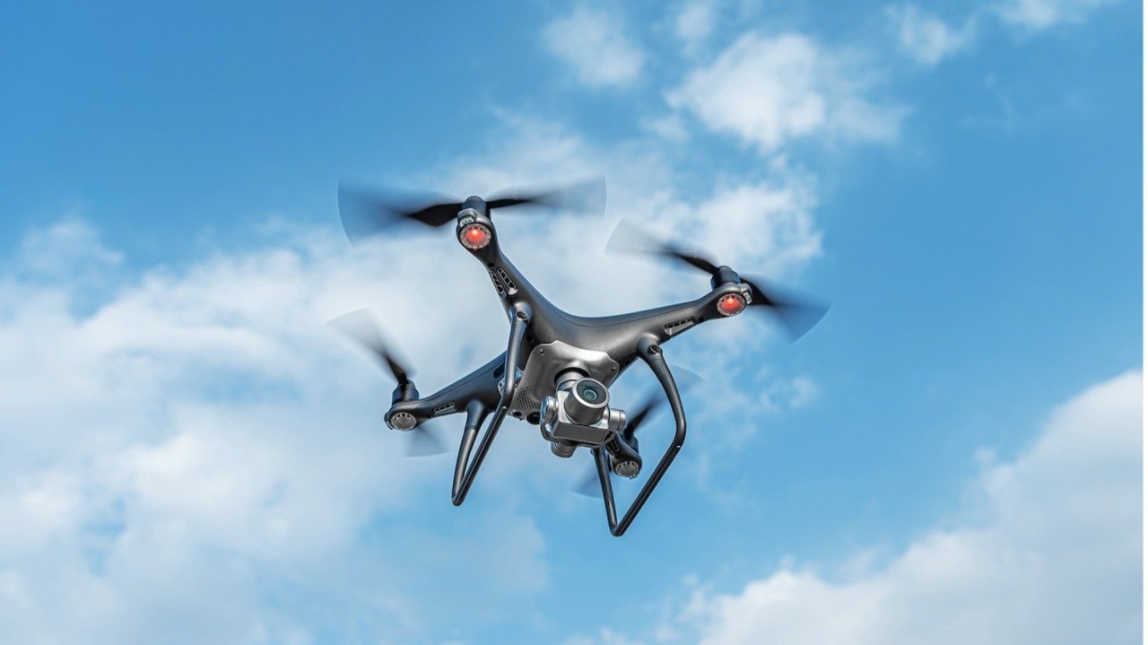 A commercial quadcopter drone flying against a blue sky with clouds