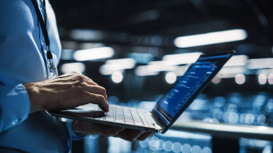 A close-up of hands typing on a laptop displaying security dashboards, in a dimly lit office environment